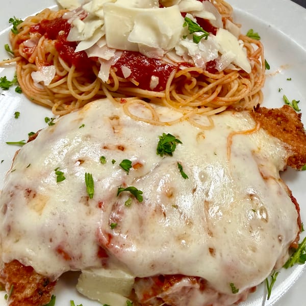 Chicken parmesan with melted mozzarella and parsley, served with spaghetti and tomato sauce.