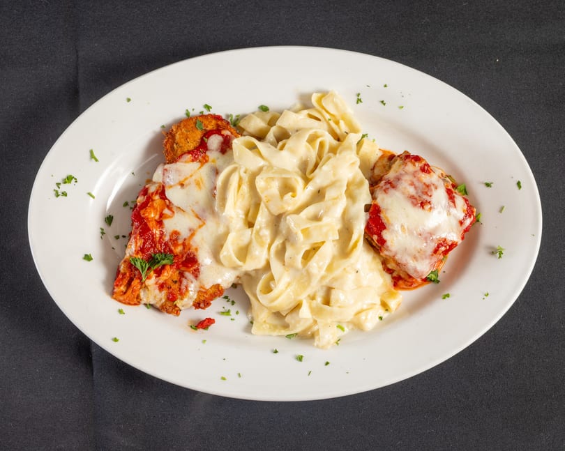Chicken parmesan with melted cheese and marinara, served with creamy fettuccine alfredo on a white plate.