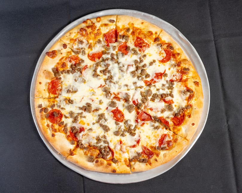 Whole pepperoni and ground meat pizza with melted cheese, sliced on a metal pan.