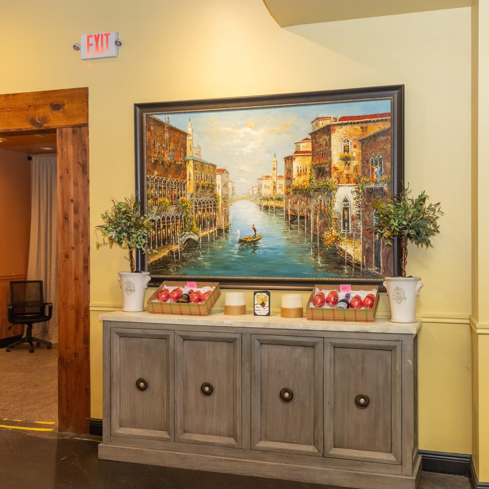 Restaurant interior with a large Venice canal painting above a cabinet displaying decorative items.