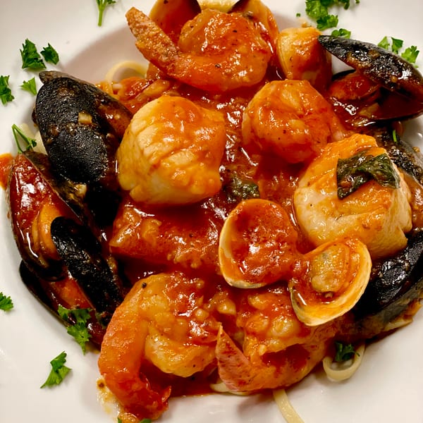 Seafood pasta with shrimp, mussels, clams, and scallops in red sauce, garnished with parsley.