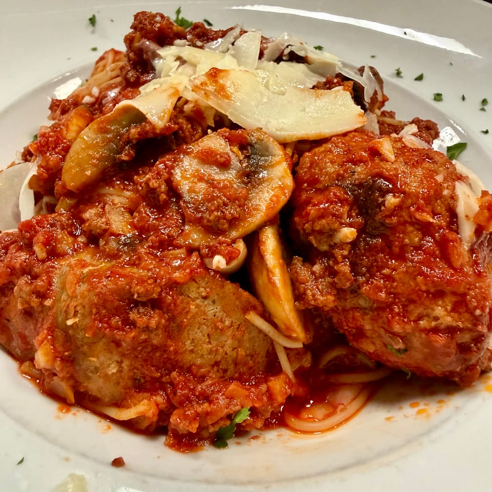 Spaghetti and meatballs with mushrooms and shaved parmesan cheese in a rich red sauce.