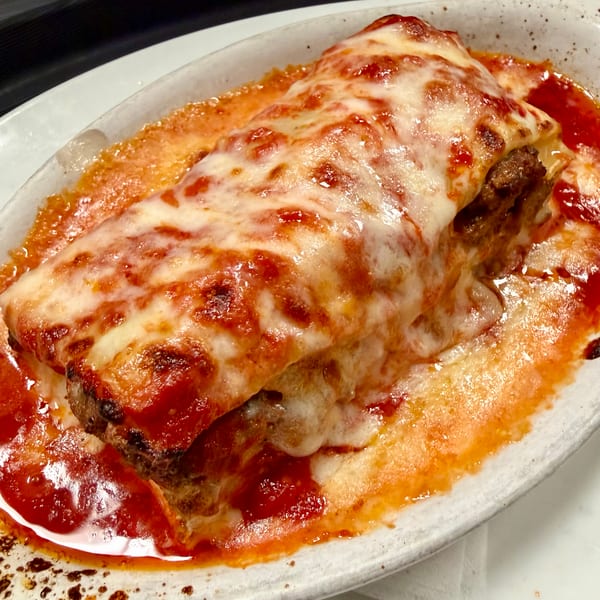 Close-up of a baked lasagna with melted cheese and rich red sauce in a white dish.