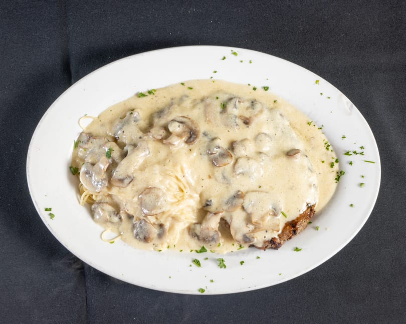 Grilled meat and spaghetti covered in a rich creamy mushroom sauce, garnished with fresh parsley.