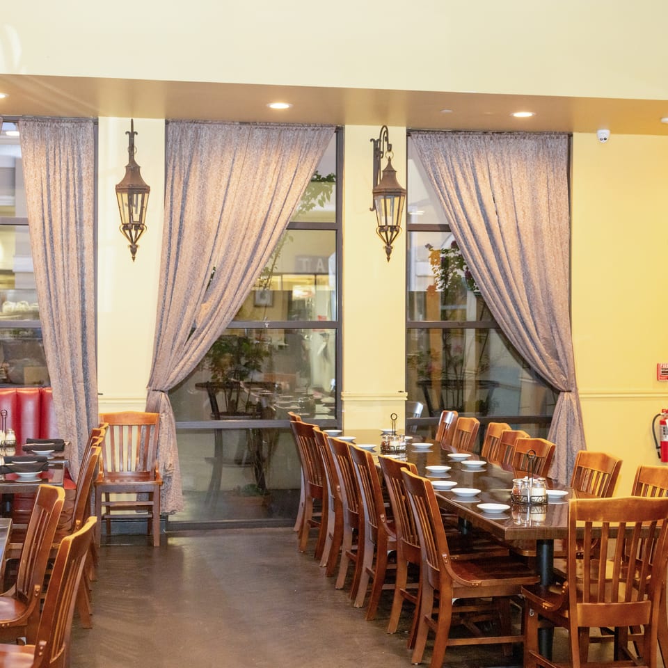 Restaurant dining room with set wooden tables, chairs, large windows, and decorative lanterns.