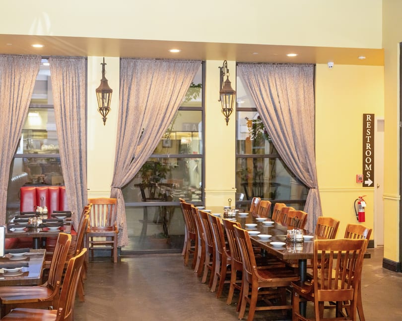 Restaurant dining room with set wooden tables, chairs, large windows, and decorative lanterns.