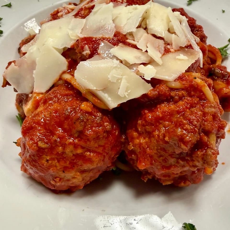 Two large meatballs covered in red sauce and shaved parmesan cheese on a white plate.