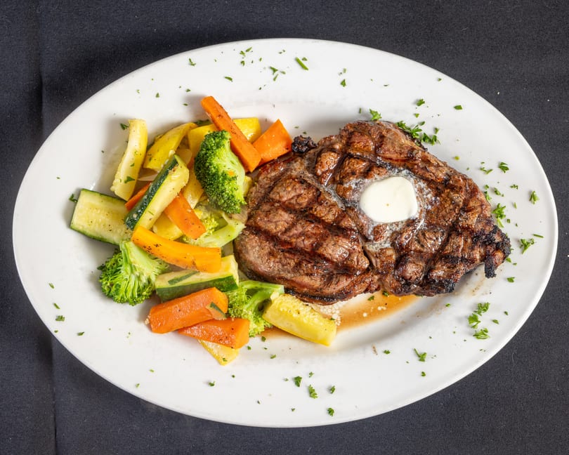Grilled steak topped with melting butter, served with steamed broccoli, carrots, zucchini, and yellow squash.