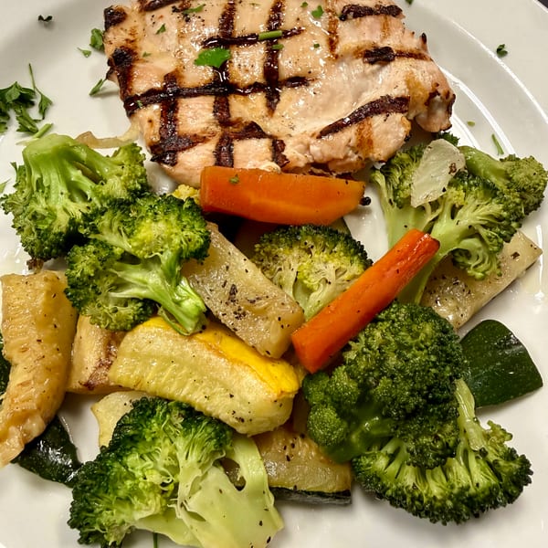 Grilled chicken breast with char marks, served alongside steamed broccoli, carrots, and squash on a white plate.