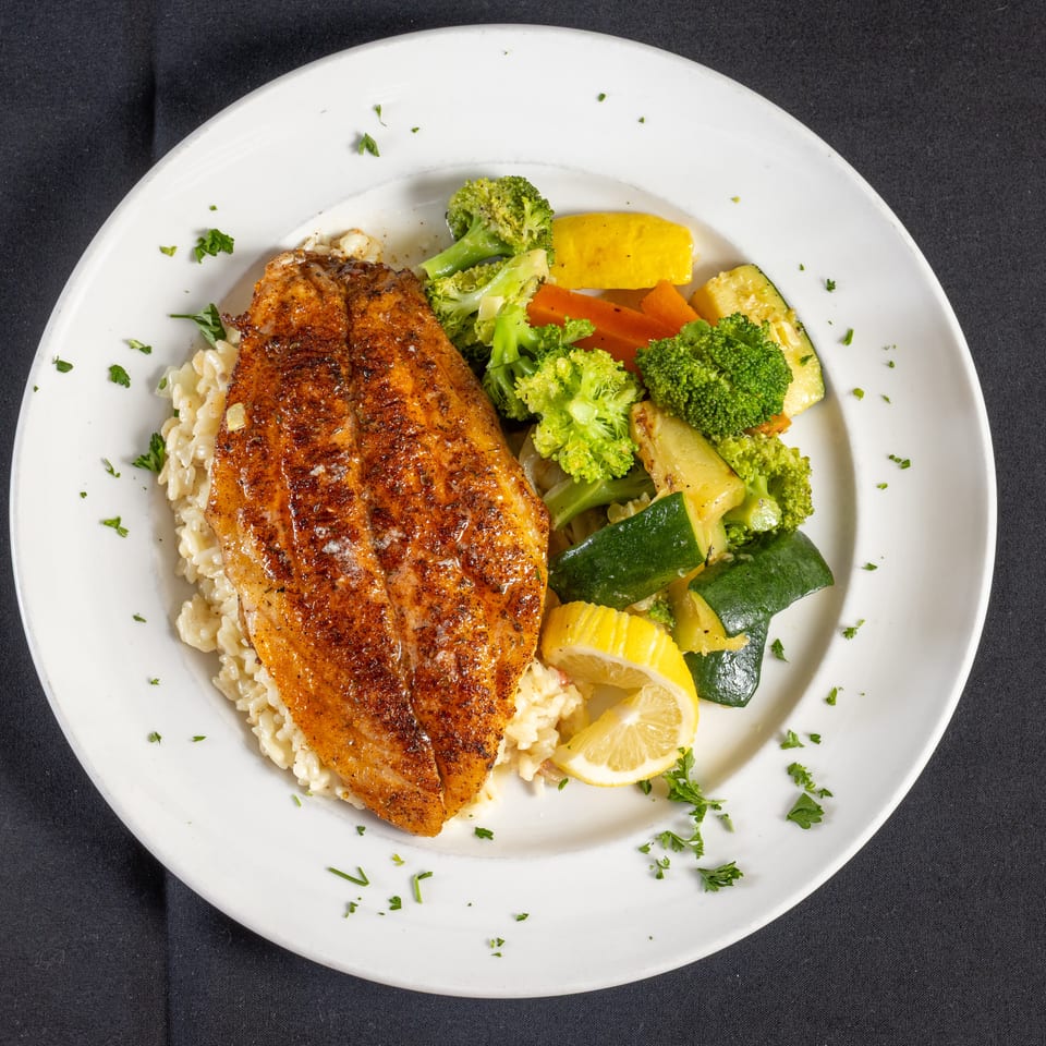Pan-seared fish with creamy rice, colorful steamed vegetables, and a lemon wedge.