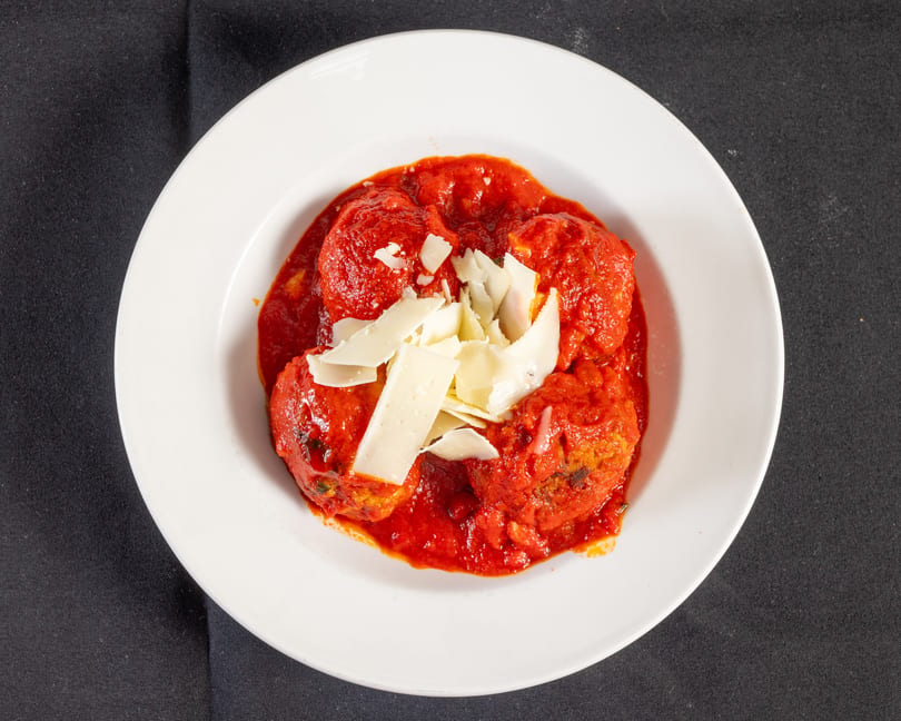 Meatballs in red sauce topped with shaved Parmesan cheese on a white plate.